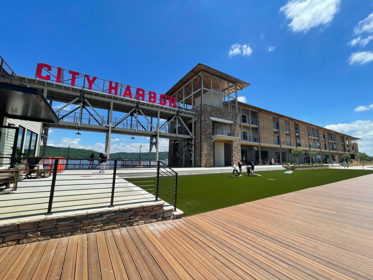 Great Southern Outdoors: Destinations for Active Travelers - 7 Modern waterfront complex with a large "CITY HARBOR" sign, outdoor seating, and a wooden boardwalkβperfect for those seeking outdoor adventure vacationsβwhere people stroll beneath a bright blue sky.