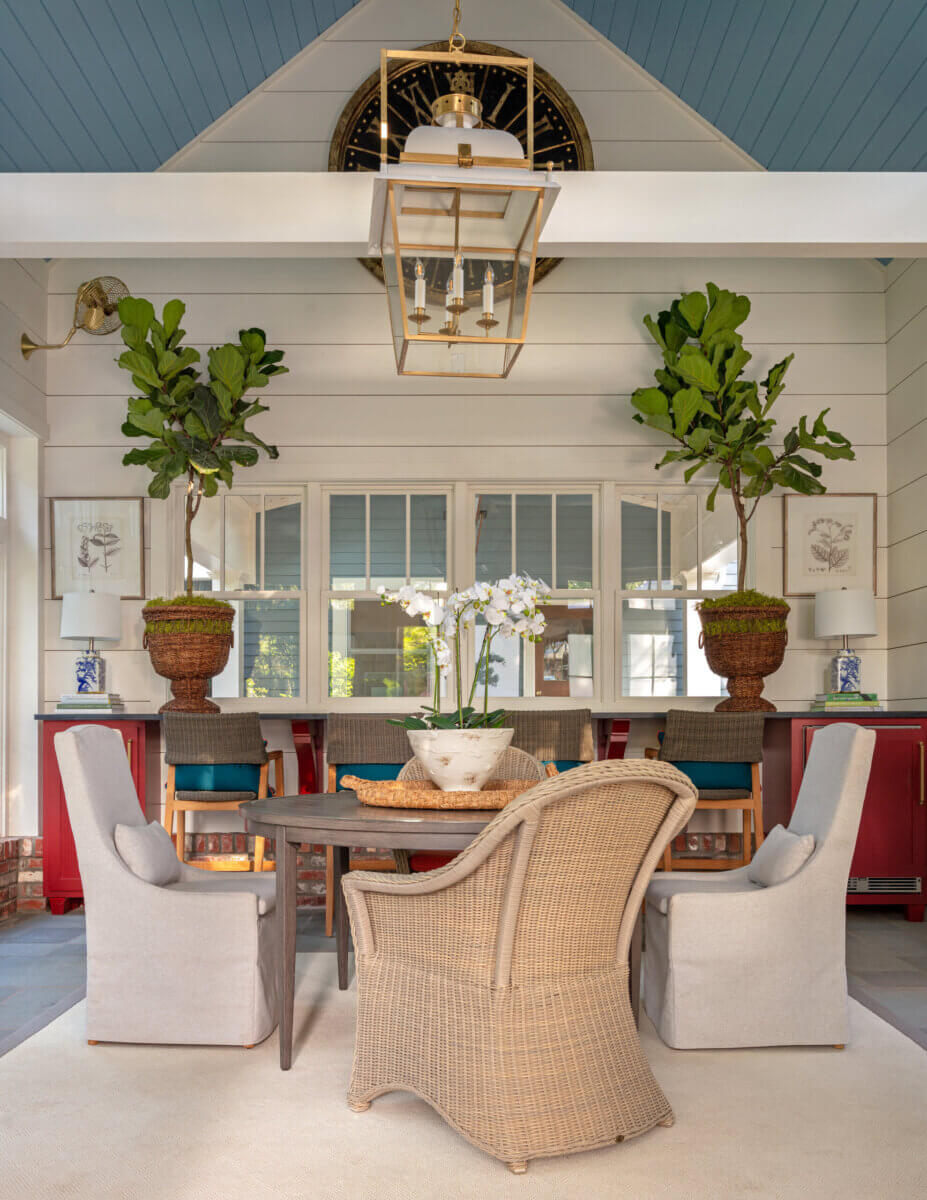Daniel Keeley on Designing Outdoor Spaces That Actually Get Used - 11 A dining area with a round table, wicker and upholstered chairs, potted plants, red cabinets, and a large lantern pendant light embodies Daniel Keeleyβs sophisticated style against white shiplap walls and a blue ceiling.