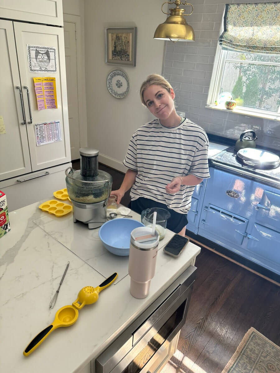 Trusting Her Gut: Meet the Charlotte Woman Making Healthy Habits Easier - 3 A woman stands in a kitchen beside a food processor and various kitchen tools on a marble island, looking at the camera.