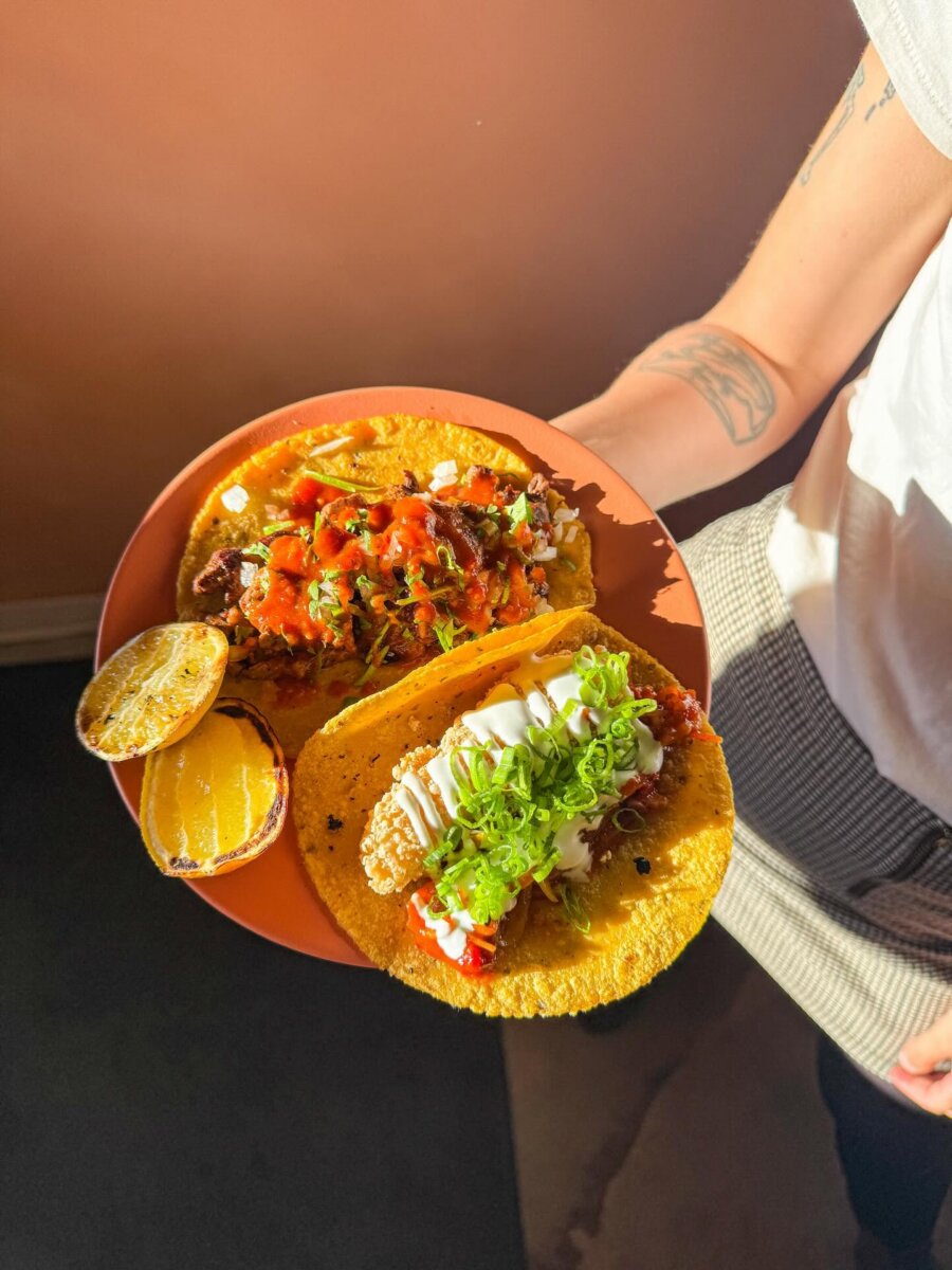 Your Guide to Sylvan Park: Nashville's Coziest Neighborhood - 4 A person holds a plate with two tacos and a grilled lime half in lively Sylvan Park; one taco has meat and red salsa, the other features a fried filling, sour cream, and chopped green onions.
