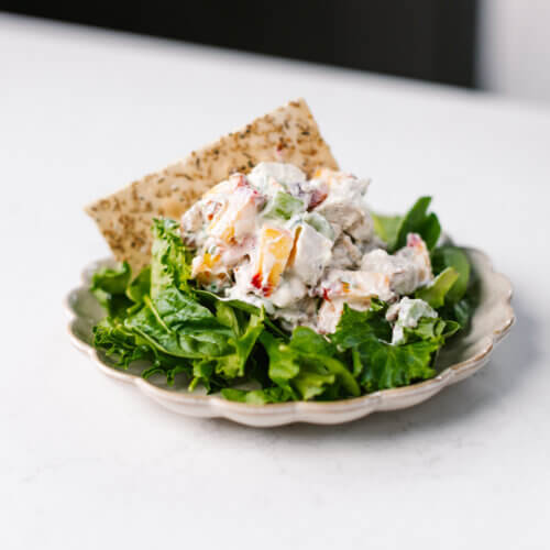 RECIPE: Peach Chicken Salad from The Peach Truck - 3 A plate with leafy greens topped with a creamy peach chicken salad and a piece of flatbread on the side.