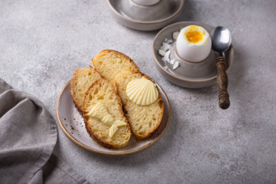 Two slices of brioche with butter on a plate, next to a soft-boiled egg in an egg cup with a spoon and salt flakes—perfect for when you want to romanticize your life with a simple breakfast ritual.