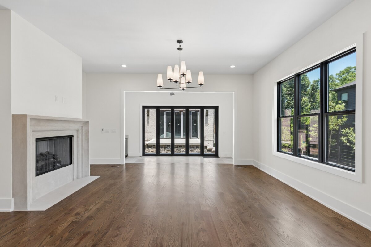 510 Stonewall Way, Brentwood TN - 1 Experience the elegance of this empty modern living room at 510 Stonewall Way, Brentwood TN, featuring hardwood floors, a white fireplace, black-framed windows, a chandelier, and glass doors leading to an inviting outdoor area.