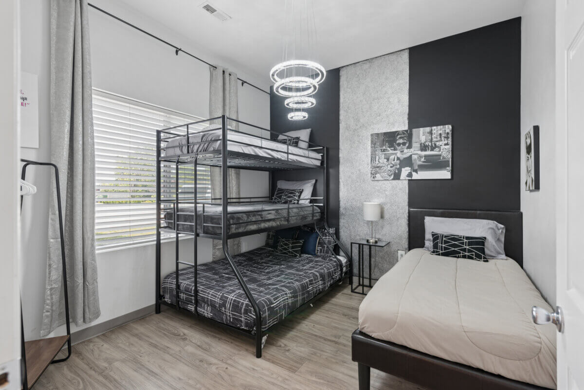Bedroom in Unit 105 & 106 at 941 Main St, Nashville, TN, featuring a twin bed and a metal-framed bunk bed, modern lighting, black accent wall, artwork, and a window with blinds.