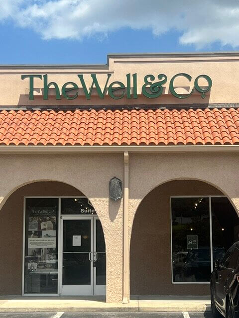 11 New Birmingham Restaurants to Try This Month - 3 Storefront of The Well & Co with large green sign, glass doors, beige exterior, and red tile roof on a sunny day.
