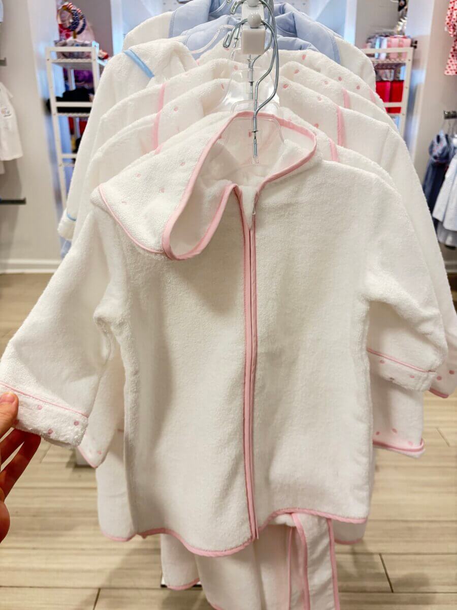 15 Birmingham FINDS for August: Breezy Fashion, Entertaining & More - 14 White infant robes with pink trim and hoods are displayed on hangers in a clothing store, a charming August FINDS collection in Birmingham.