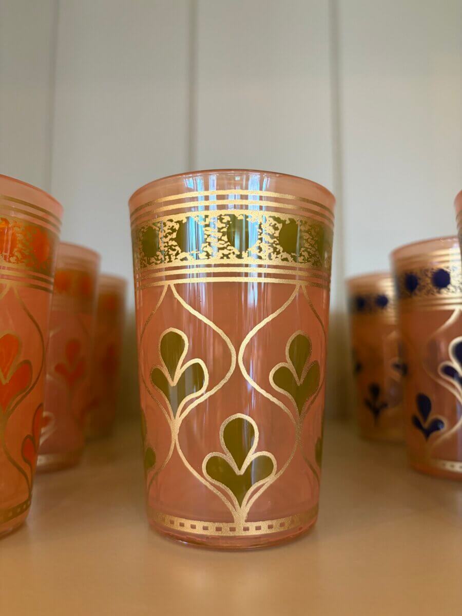 15 Birmingham FINDS for August: Breezy Fashion, Entertaining & More - 2 A pink glass with gold and green decorative patterns is displayed on a shelf at August FINDS in Birmingham, surrounded by similar glasses in the background.