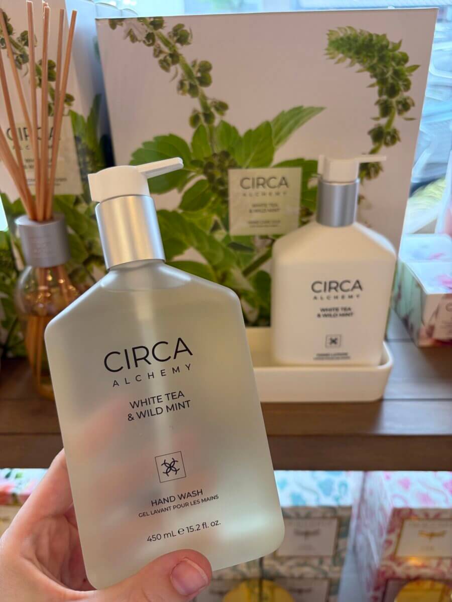 15 Birmingham FINDS for August: Breezy Fashion, Entertaining & More - 11 A hand holds a bottle of Circa Alchemy White Tea & Wild Mint hand wash in front of matching Circa products on a store shelf—one of our favorite August FINDS spotted in Birmingham.