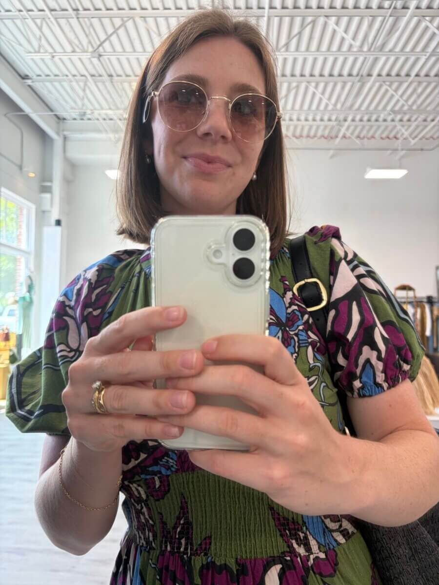15 Birmingham FINDS for August: Breezy Fashion, Entertaining & More - 8 A woman wearing sunglasses takes a selfie indoors in Birmingham, holding a white phone and wearing a patterned dress as she finds herself enjoying the style of August.