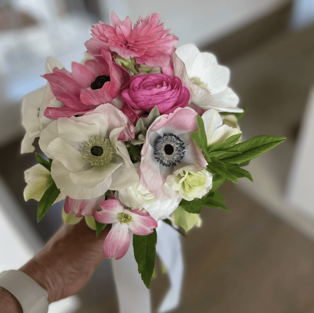 5 U-Pick Flower Farms Near Birmingham - 2 A hand holds a small bouquet of pink and white flowers from a Birmingham U-Pick Flower Farm, with green leaves against a blurred indoor background.
