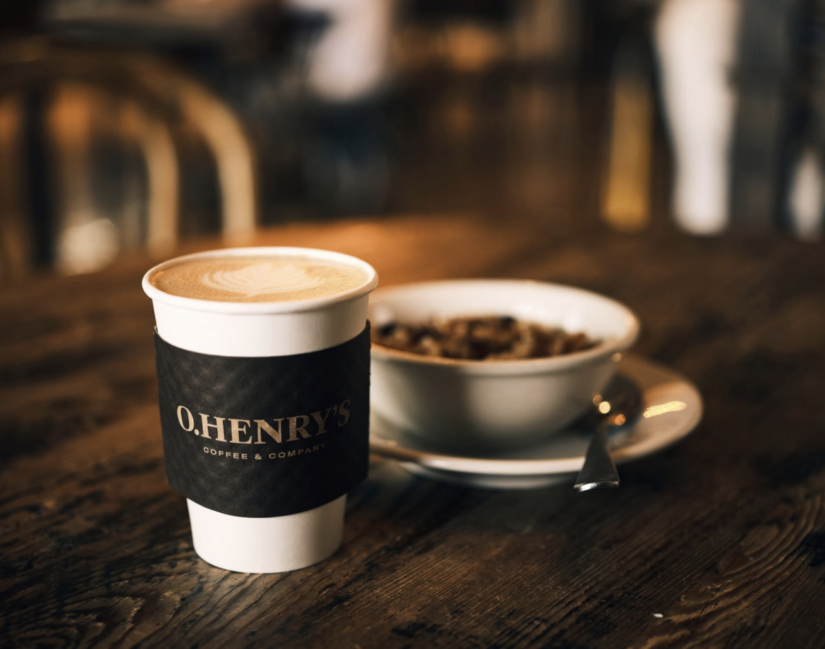 Your Guide to BHAM's Charming Highland Park Neighborhood - 2 A cup of coffee with an O.Henry’s sleeve sits next to a bowl of cereal with a spoon on a rustic wooden table in a cozy Highland Park cafe, the perfect spot for starting your day in BHAM’s most charming neighborhood guide.