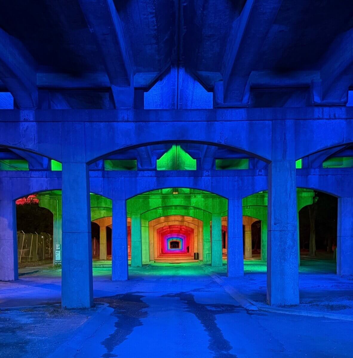 Concrete underpass at night, illuminated with blue, green, and red lights, creating a colorful, tunnel-like effect—a dramatic makeover.
