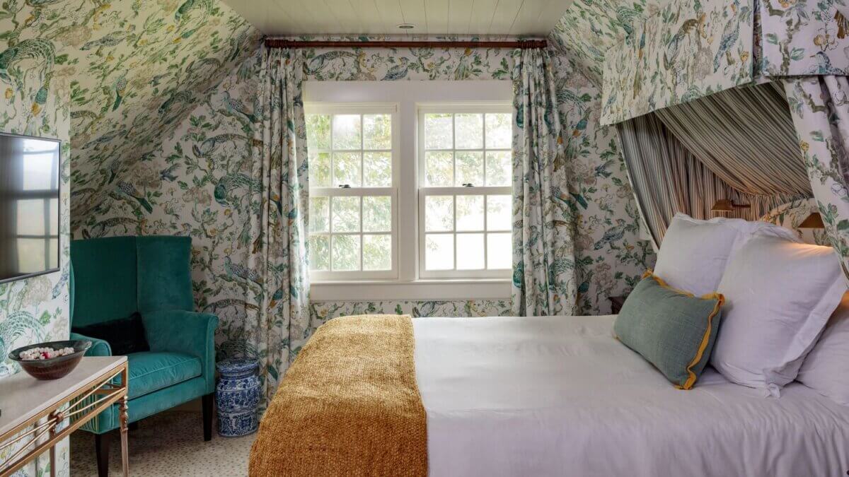 8 Luxurious, Family-Friendly Resorts in the South - 8 Bedroom with patterned wallpaper, a bed with white linens and a gold blanket, green armchair, window with curtains, and a TV on the wall—this inviting space captures the warmth and comfort often found in family-friendly resorts ideal for Southern families.