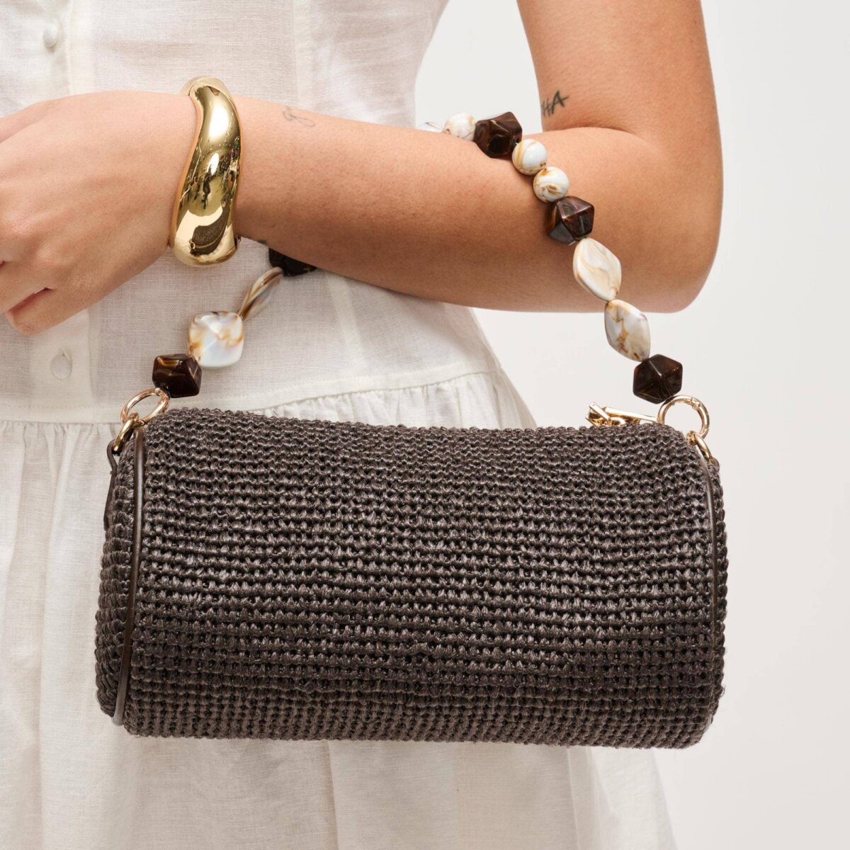 A person in a white dress holds a cylindrical woven black handbag with a chunky beaded strap—one of the standout August FINDS in Nashville—and wears a gold bracelet.
