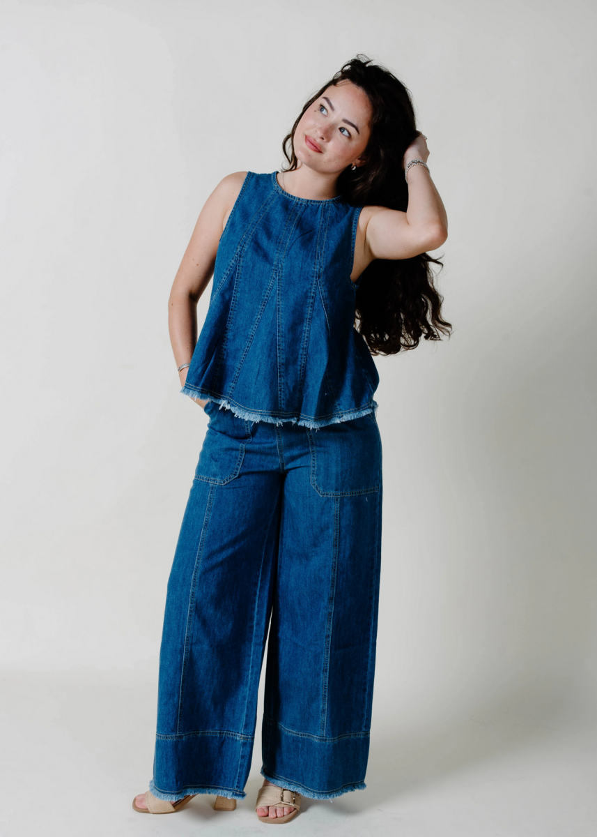Woman in sleeveless denim top and wide-leg denim pants stands on a plain background, looking to the side with one hand touching her hair—embodying effortless August style inspired by Nashville FINDS.
