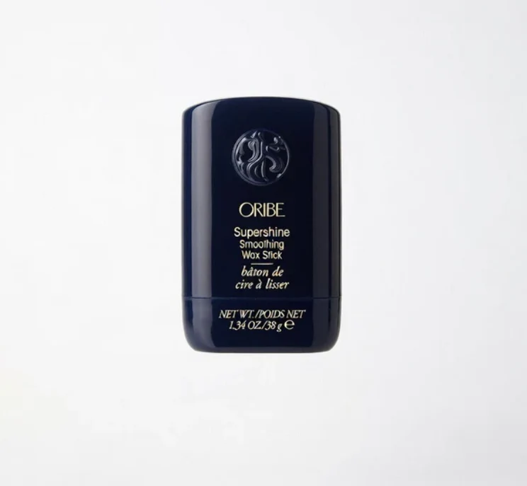 A dark blue container of Oribe Supershine Smoothing Wax Stick, 1.34 oz, is shown standing upright against a plain white background.