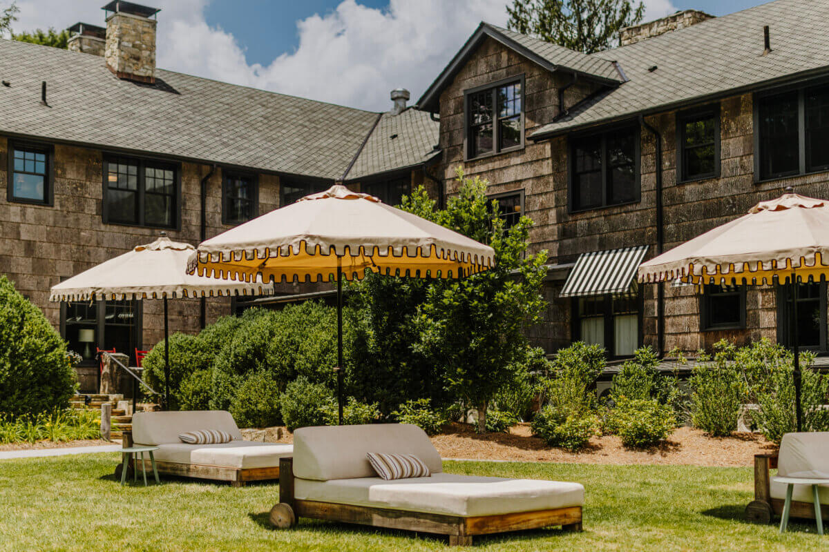 8 Luxurious, Family-Friendly Resorts in the South - 5 Outdoor lounge chairs and umbrellas are set on a grassy area in front of a large stone building with multiple windows and greenery, creating an inviting space perfect for Southern families seeking relaxing moments at family-friendly resorts.