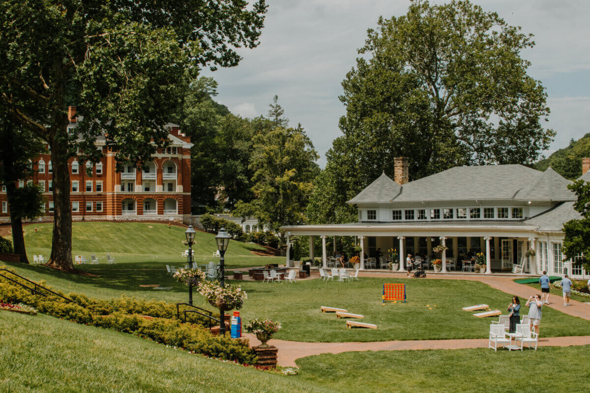 8 Luxurious, Family-Friendly Resorts in the South - 3 A large grassy courtyard with lawn games, white chairs, a patio building, and a red brick building in the background, surrounded by trees on a sunny day—this inviting setting captures the charm of Family-Friendly Resorts, offering an ideal escape for Southern Families to relax and play together.