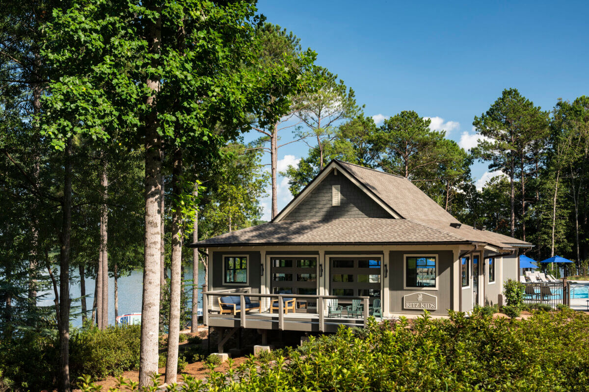 8 Luxurious, Family-Friendly Resorts in the South - 17 A small, family-friendly house with large windows sits surrounded by trees near a lake—perfect for Southern families seeking a peaceful retreat—with a wooden deck and outdoor seating visible in the foreground.
