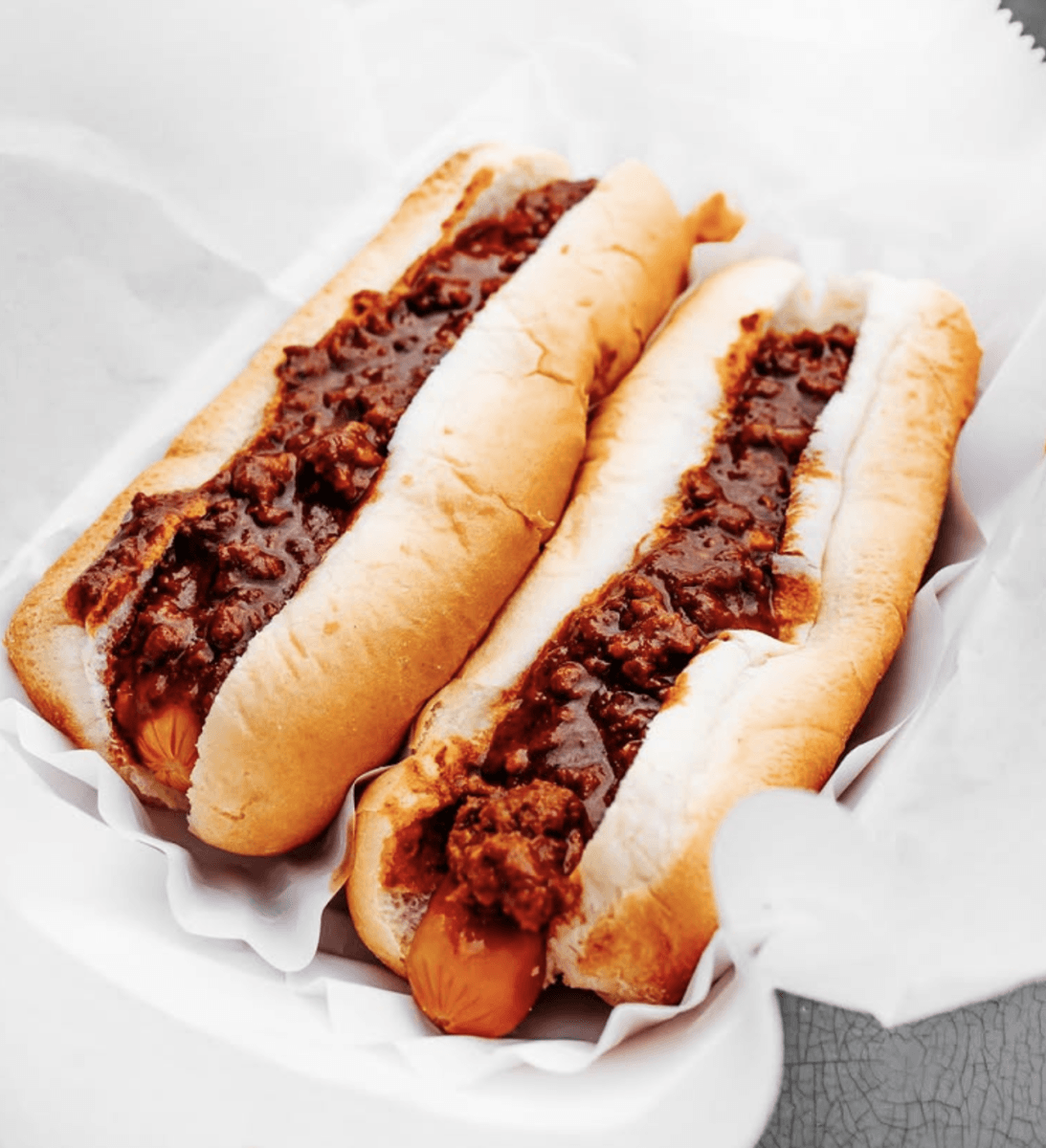6 Louisville Hot Dogs Worth the Hype - 5 Two hot dogs in buns topped with chili are placed side by side in a white paper tray with a white paper liner.