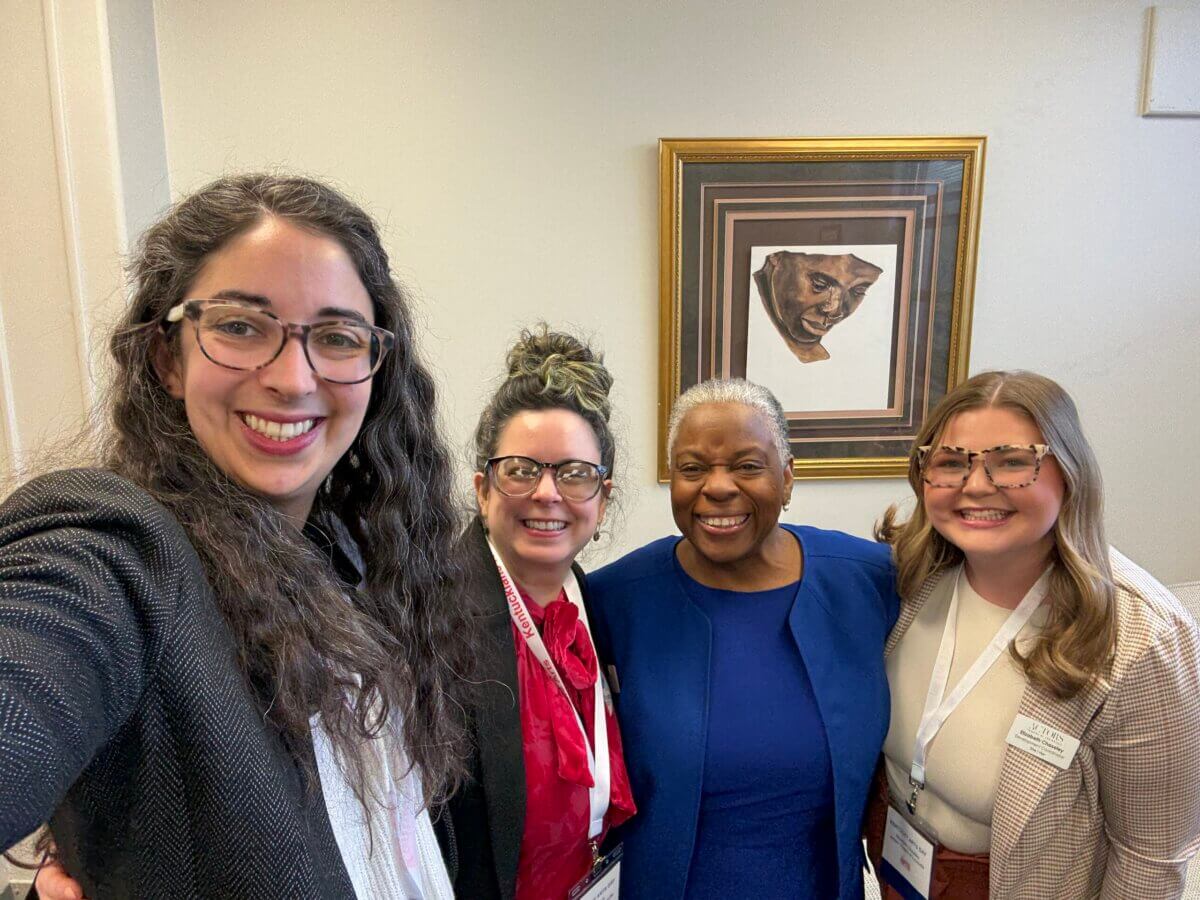 Meet the Creative Visionary Behind Actors Theatre of Louisville - 4 Four women standing together and smiling indoors at the Actors Theatre of Louisville, with one taking a selfie. A framed portrait hangs on the wall behind them.