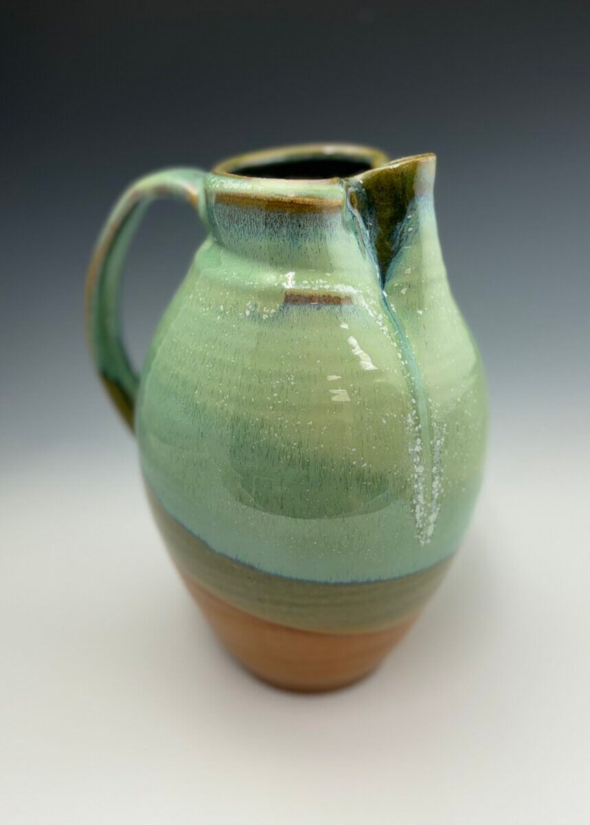 Meet the Louisville Artist Behind Payne Street Pottery - 7 Handcrafted by a skilled Louisville potter, this ceramic pitcher features a round body, green and brown glazing, a wide handle, and a spout, set against a neutral background.