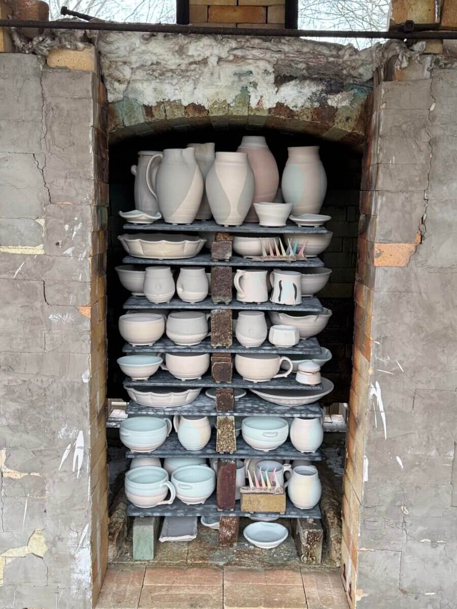 Meet the Louisville Artist Behind Payne Street Pottery - 5 Open kiln filled with unglazed ceramic pots, plates, bowls, and cups stacked on shelves—each piece shaped by clay and creativity from the Louisville Potter community. The kiln has a rustic brick exterior, with some tools placed on the bottom.