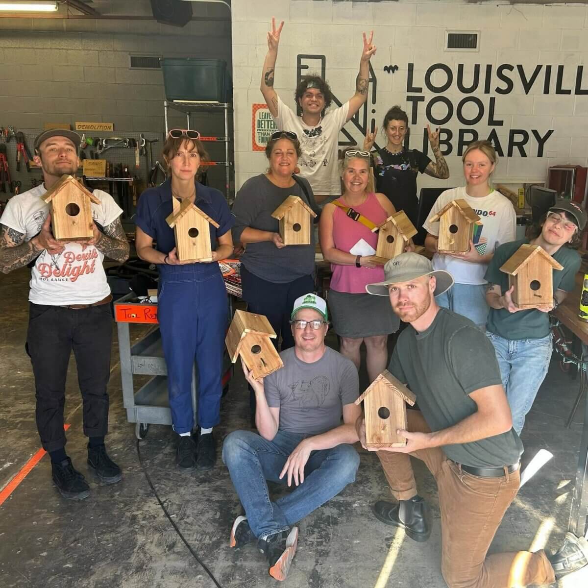 Shelf Help: Louisville's Tool Library Has You Covered - 3 A group of people in a workshop hold up wooden birdhouses they made, posing and smiling at the Louisville Tool Libraryβa hub for creativity and tool lending in the community.