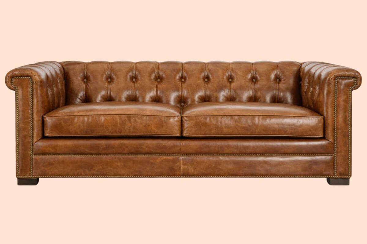 16 Luxe Louisville FINDS for July: Fine Art, Rare Bourbon & Resort-Ready Style - 2 Brown leather Chesterfield sofa with tufted backrest, rolled arms, and nailhead trim, featured as part of Louisville Finds July, set against a plain light beige background.