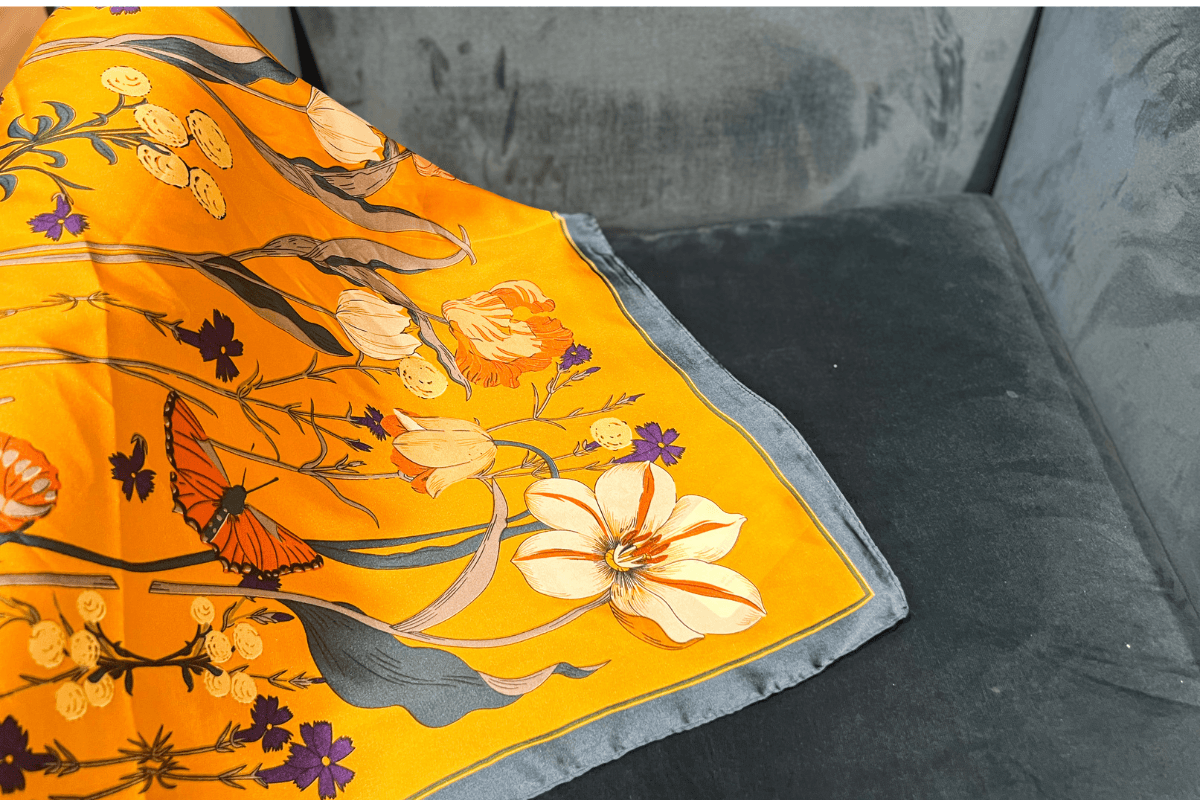 20 Memphis FINDS to See You Through the End of Summer - 12 A yellow floral scarf with a butterfly design is draped over the corner of a gray velvet sofa.