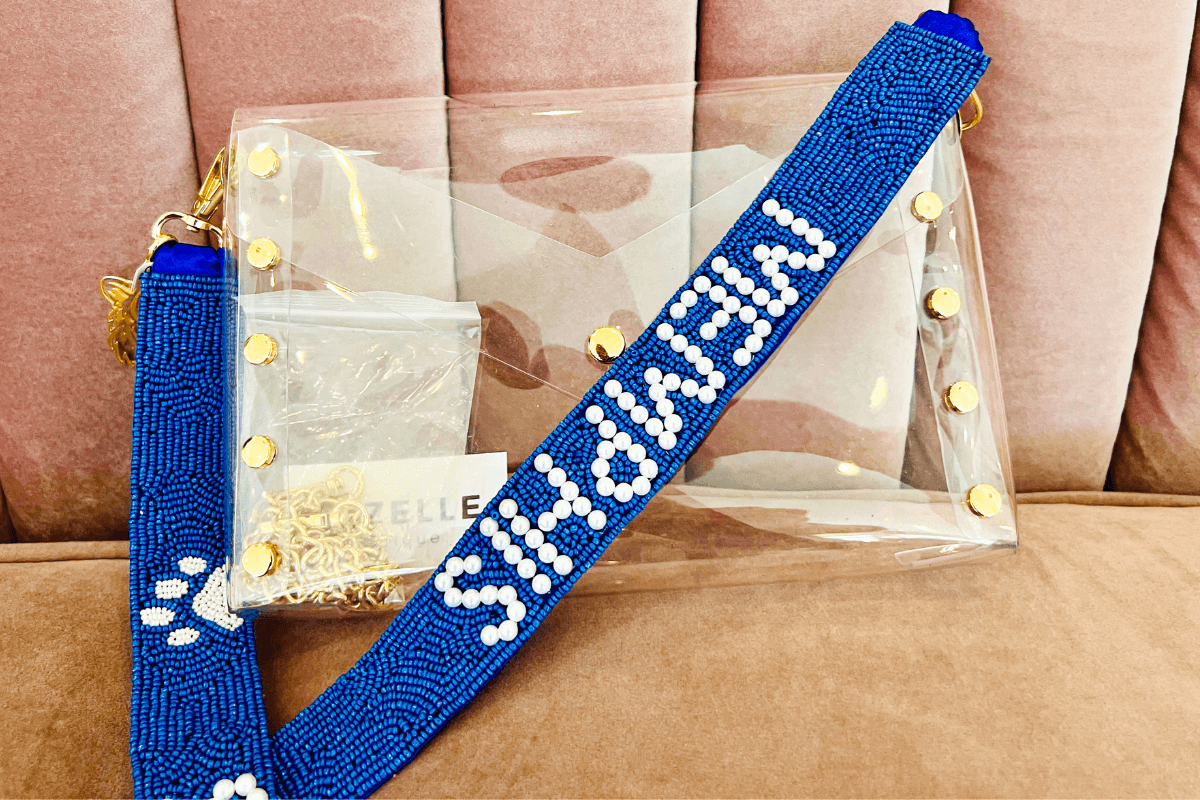 20 Memphis FINDS to See You Through the End of Summer - 10 Clear purse with gold studs and a blue beaded strap that reads "MEMPHIS," displayed on a pink cushioned surface.