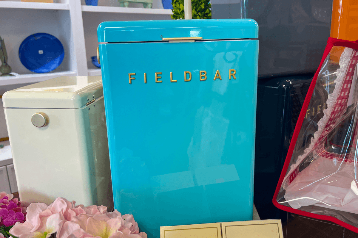 20 Memphis FINDS to See You Through the End of Summer - 2 A turquoise FIELDBAR cooler is displayed on a shelf with other coolers and decorative items, including flowers and glassware, in the background.