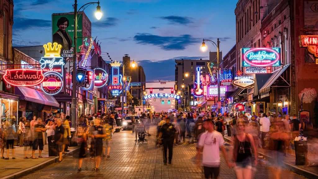 16 Free Things to Do in Memphis - 4 A busy street scene at dusk with crowds walking among vibrant neon signs, bars, and restaurants in a lively entertainment district.