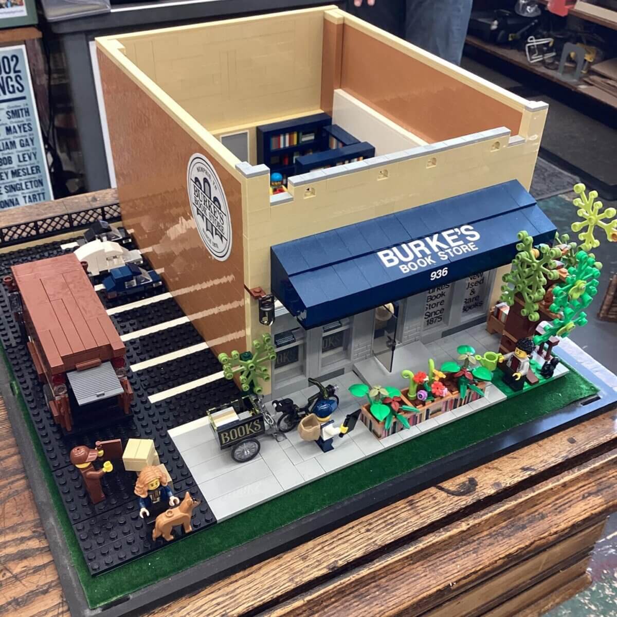 LEGO model of a bookstore named "Burke's Book Store" with a blue awning, street details, figures, books, and a delivery area in the back.