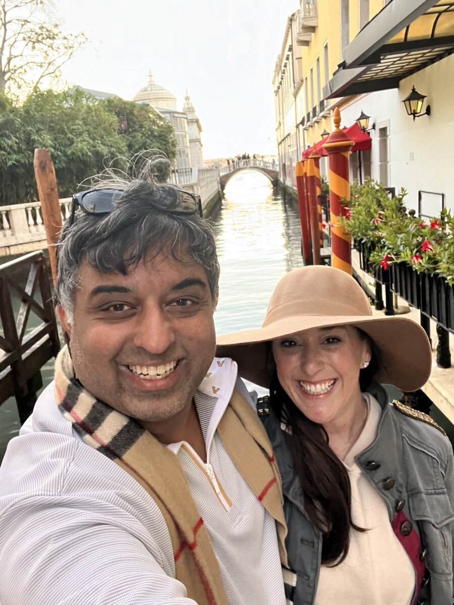 She's Building Memphis's Newest Stomping Grounds - 6 Lindsey Shanmugasundaram and her husband smile for a selfie in front of a canal as a charming bridge and colorful buildings provide the perfect backdrop on a clear day.