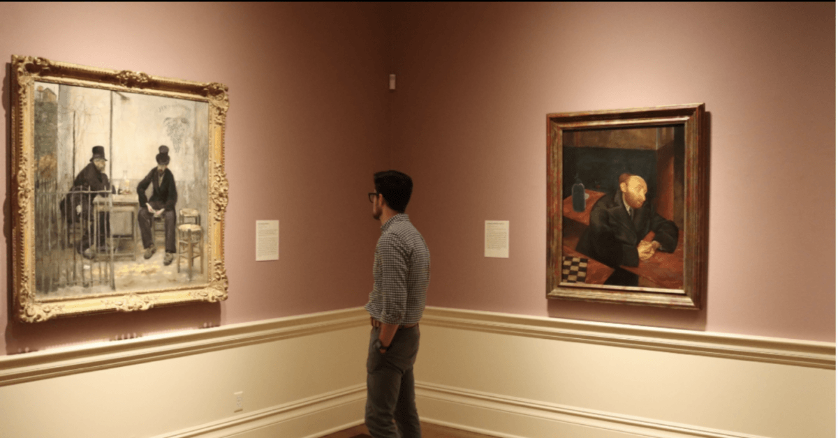 16 Free Things to Do in Memphis - 3 A man stands in an art gallery, observing two framed paintings displayed on adjacent walls with informational plaques beside them.