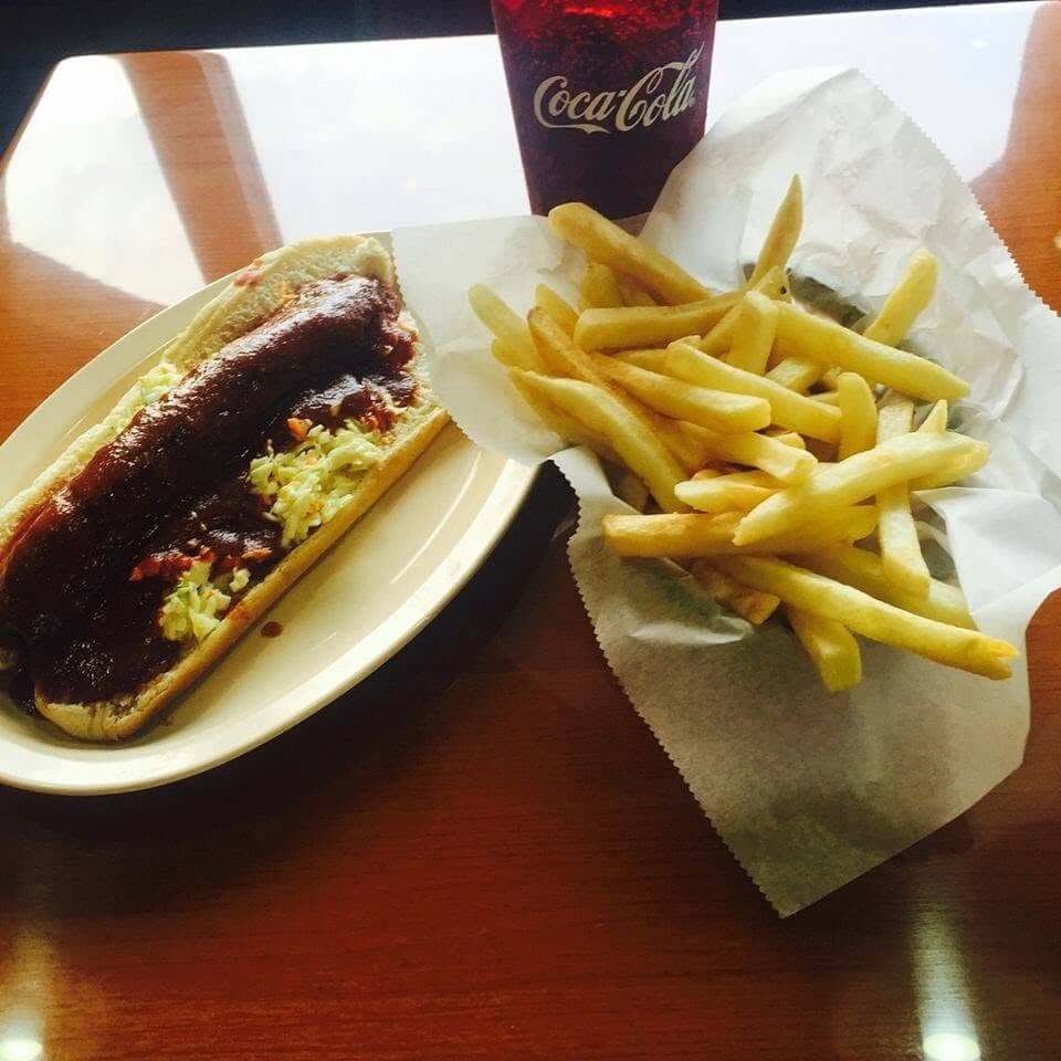 8 Memphis Hot Dogs That Go Way Beyond the Basics - 7 A hot dog with coleslaw and barbecue sauce is served on a plate next to a basket of French fries and a cup of Coca-Cola on a wooden table.