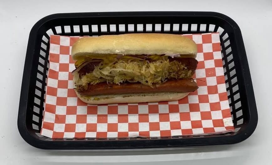 8 Memphis Hot Dogs That Go Way Beyond the Basics - 5 A hot dog with sauerkraut and other toppings in a bun, served in a black basket lined with red and white checkered paper.