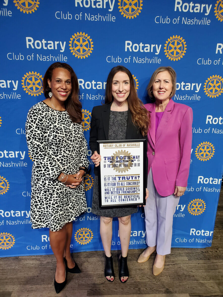 She’s Helping Put Books in the Hands of 500,000 Tennessee Kids - 4 Three women stand in front of a Rotary Club of Nashville backdrop. The woman in the center holds a framed Rotary Club "Four-Way Test" sign.