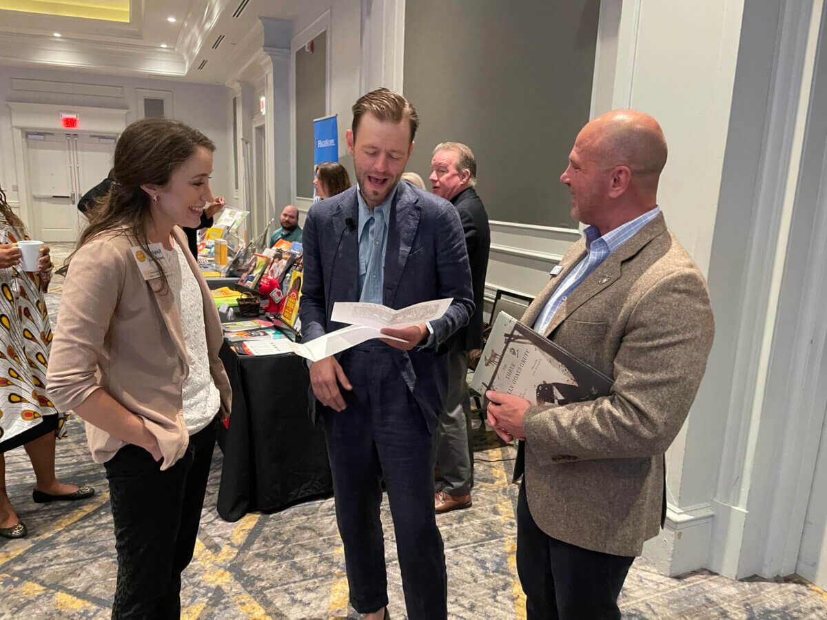 She’s Helping Put Books in the Hands of 500,000 Tennessee Kids - 6 Three people stand talking in a conference room, discussing Tennessee education initiatives. One person holds papers, another holds a folder, and a display table with snacks is visible in the background.