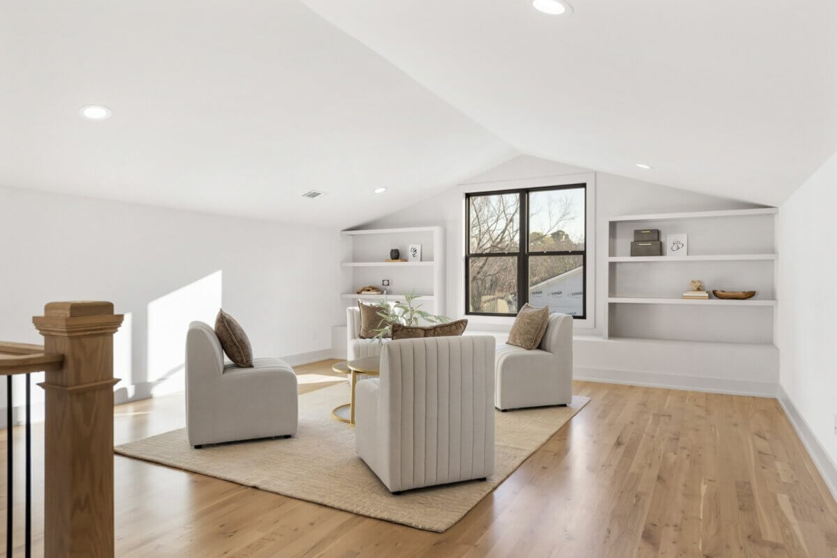 A Look Inside Brentwood's Newest Luxury Address - 11 Bright loft space with wood floors, three white armchairs around a round table, built-in shelves, large window, and neutral decor—an inviting interior often featured among Nashville luxury homes for sale.