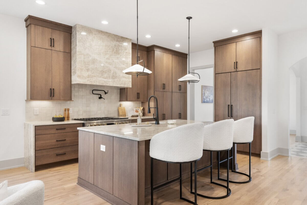 A Look Inside Brentwood's Newest Luxury Address - 5 Modern kitchen with wood cabinets, marble island and countertops, three white barstools, pendant lights, and stainless steel appliances—perfect for those seeking the sophisticated style found in Nashville luxury homes for sale.