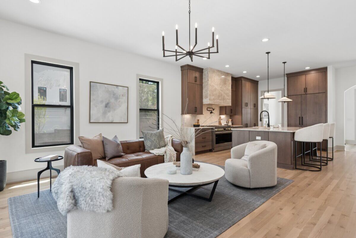 A Look Inside Brentwood's Newest Luxury Address - 4 Modern open-concept living room and kitchen with brown cabinets, a leather sofa, two armchairs, a round coffee table, and neutral decor—perfect for those seeking Nashville luxury homes for sale.