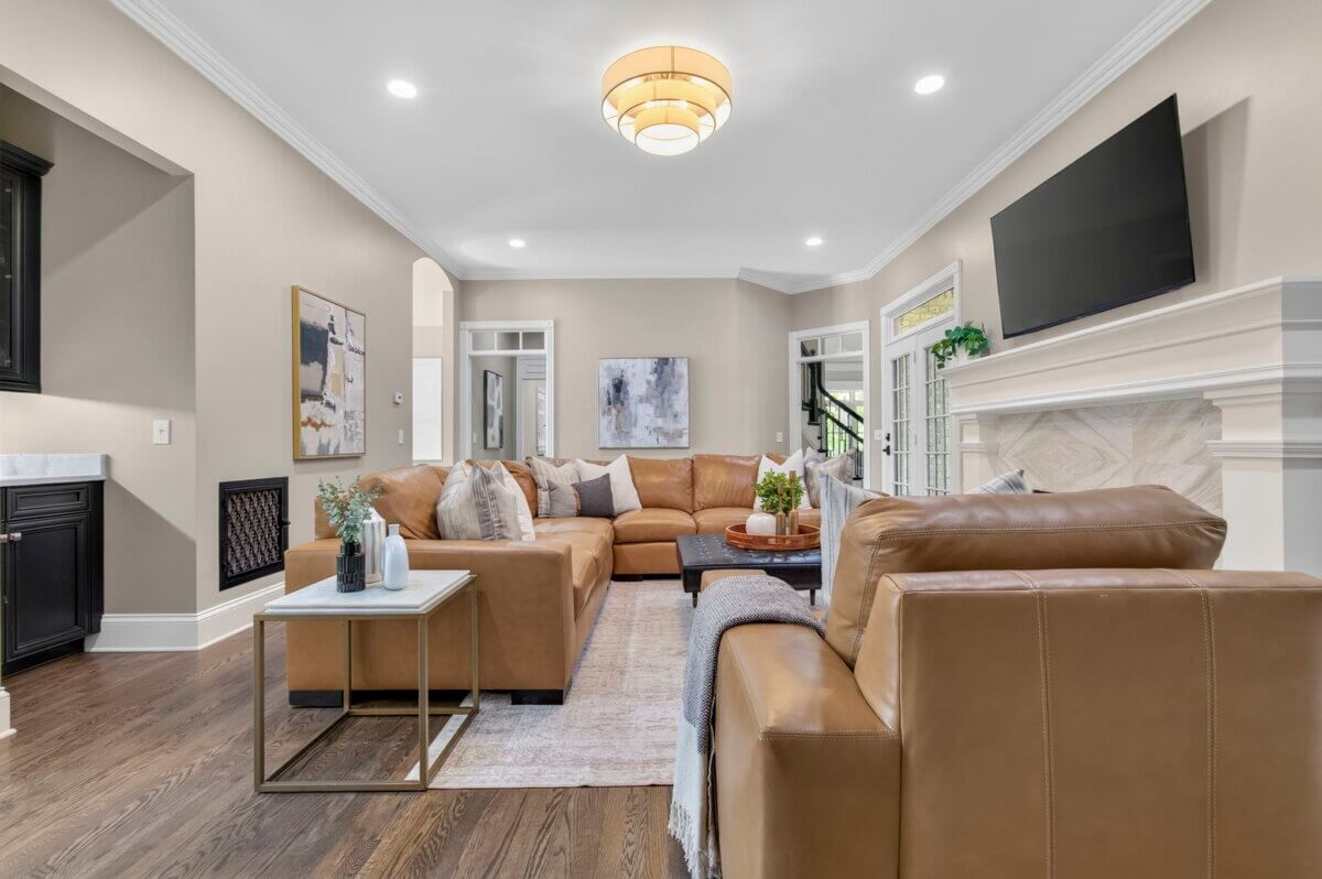 Modern living room in a Brentwood Entertainer's Dream Home, featuring tan leather sofas, a wall-mounted TV above a white fireplace, hardwood floors, and decorative artwork on neutral-colored walls—perfect for those seeking luxury real estate.