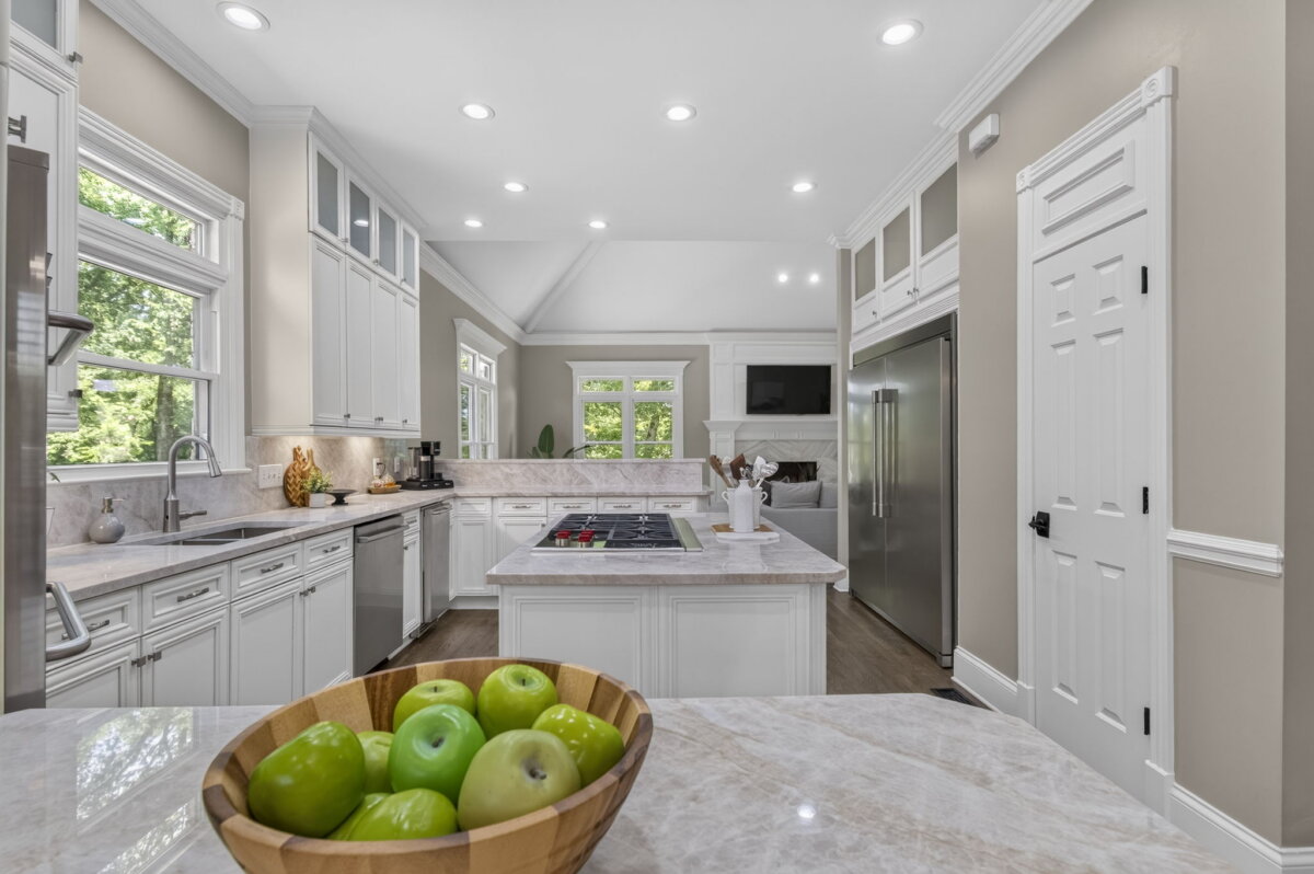 Just Listed! This Renovated Brentwood Home Has a Private Primary Wing, 4 Fireplaces & a Park-Like Backyard - 9 Modern Brentwood Home kitchen with white cabinets, stainless steel appliances, and a marble countertop featuring a wooden bowl of green apples in the foreground. This beautifully renovated space overlooks a park-like backyard, creating an inviting atmosphere for both cooking and entertaining.