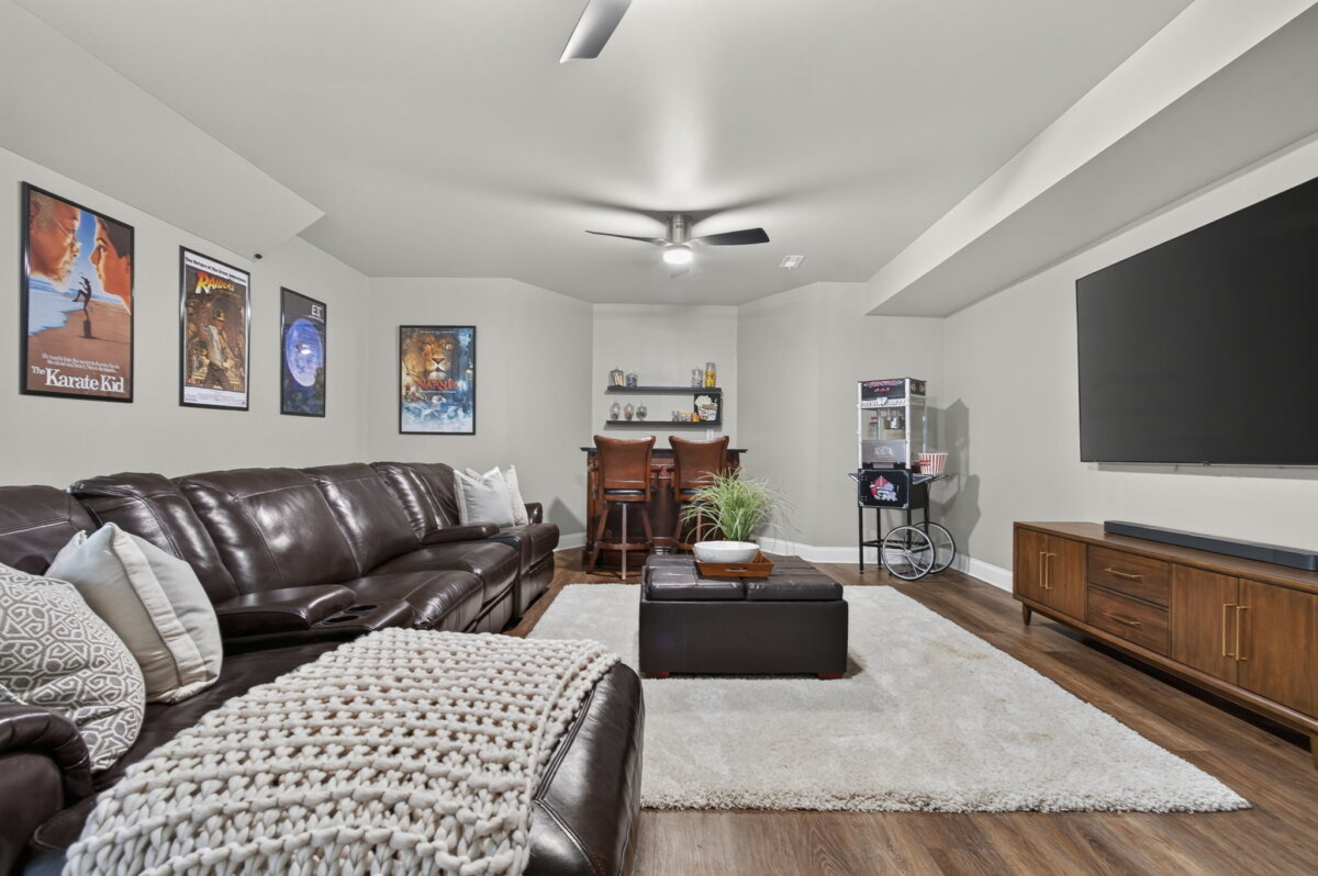 Just Listed! This Renovated Brentwood Home Has a Private Primary Wing, 4 Fireplaces & a Park-Like Backyard - 17 Basement media room with brown leather sofas, a white rug, a large TV, movie posters on the walls, a bar area with stools, and a popcorn machineβperfect for relaxing after enjoying the park-like backyard of this renovated Brentwood home.