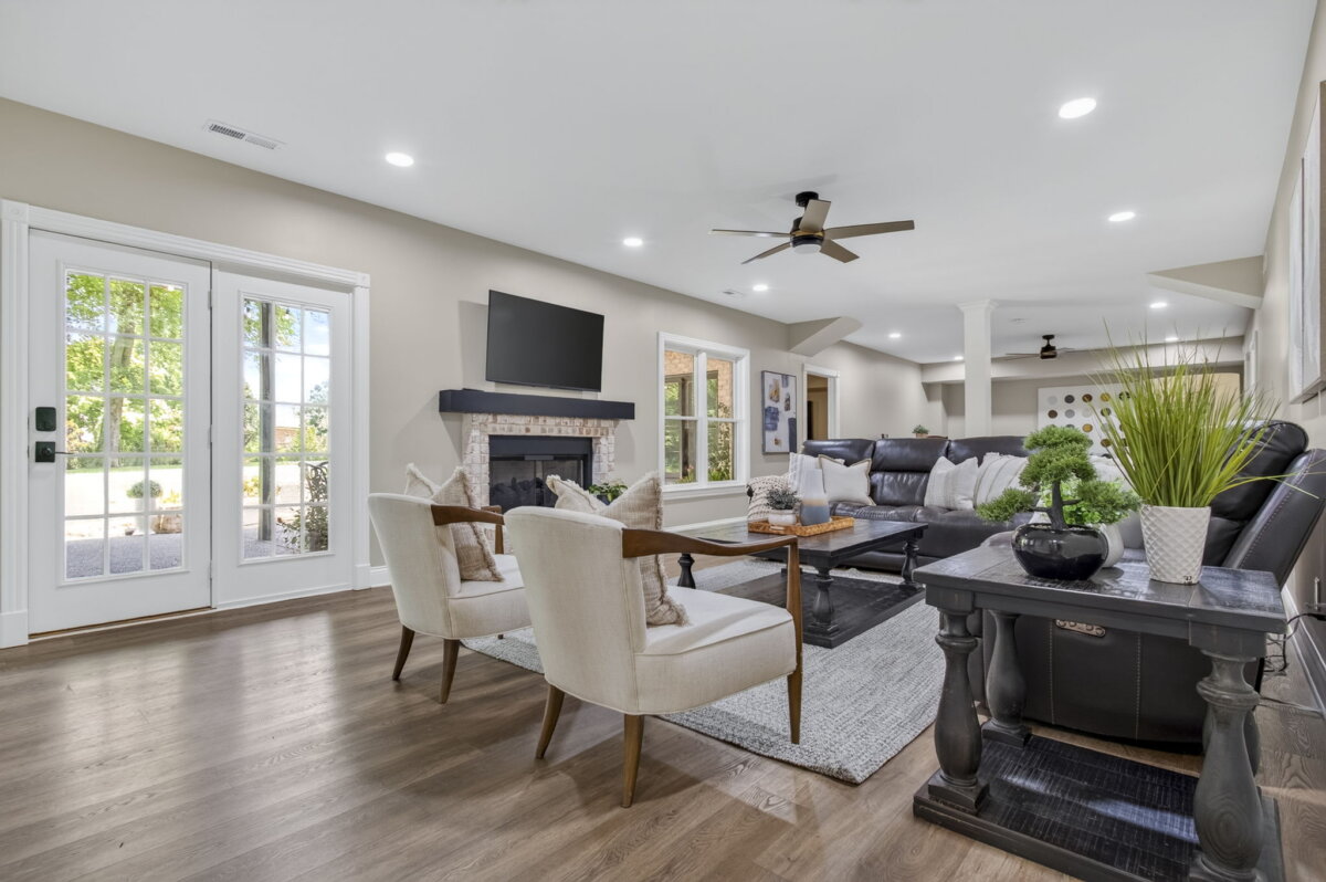 Just Listed! This Renovated Brentwood Home Has a Private Primary Wing, 4 Fireplaces & a Park-Like Backyard - 16 Modern living room with neutral walls, wood floors, a fireplace, a wall-mounted TV, a black sofa, two white chairs, a coffee table, and large windows letting in natural lightβperfectly embodying the comfort and elegance of this renovated Brentwood home.