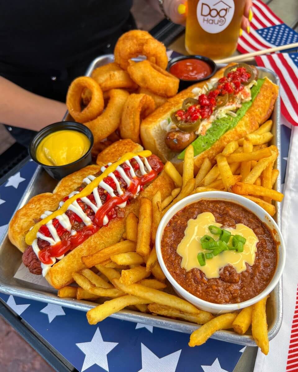 A tray with fries, chili cheese, onion rings, and two loaded hot dogs—classic essential hot dog orders for any Nashville food lover. One hot dog has ketchup and mayo, the other is topped with guacamole and salsa.