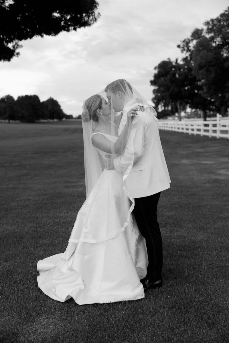 This Dreamy Equestrian Wedding Made History at Franklin's Harlinsdale Farm - 7 A bride and groom stand on a lawn at Harlinsdale Farm in Franklin, embracing and facing each other, both dressed in wedding attire with the bride wearing a veil.