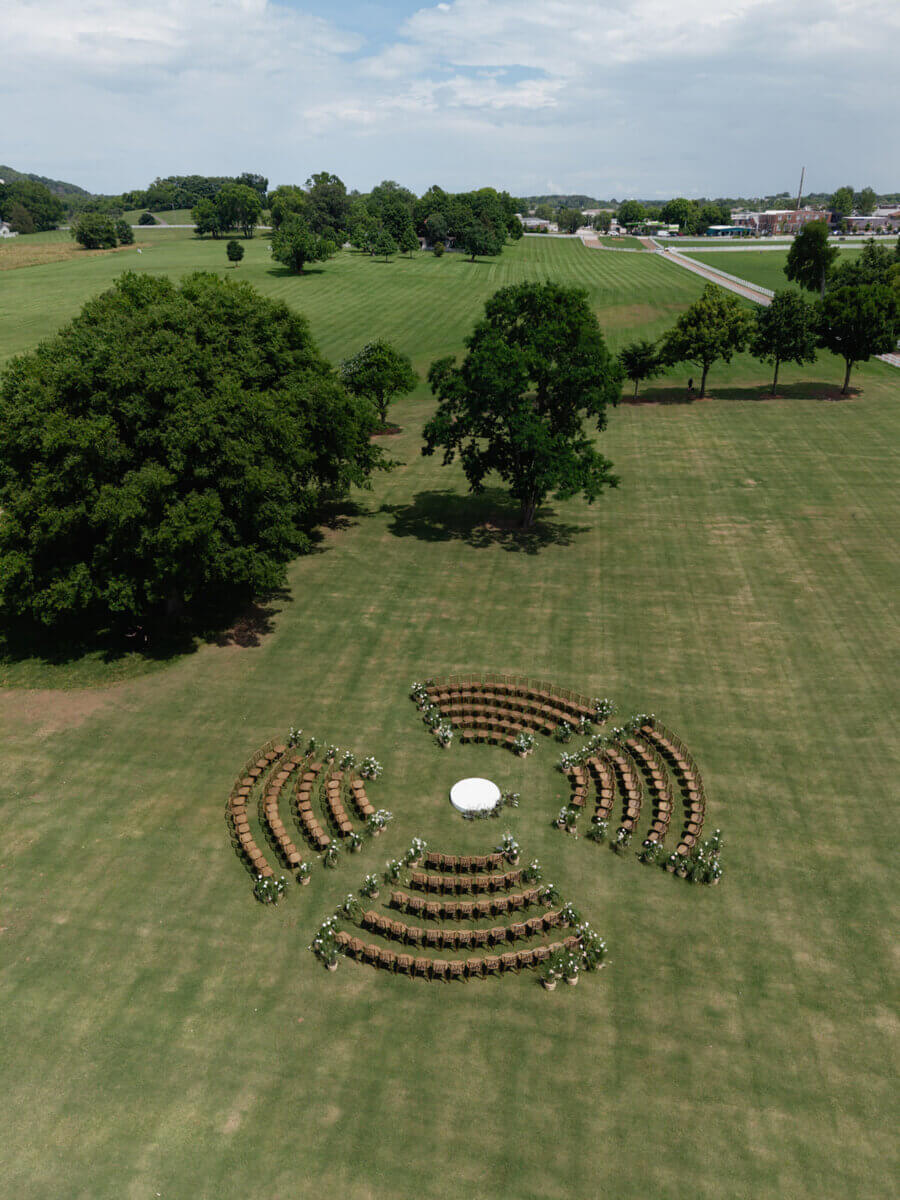 This Dreamy Equestrian Wedding Made History at Franklin's Harlinsdale Farm - 10 Aerial view of a circular outdoor seating arrangement with rows of chairs and a central table, set up on the expansive grassy fields of Harlinsdale Farm in Franklin, perfect for an elegant wedding surrounded by trees.